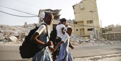 School children walk through rubbled streets